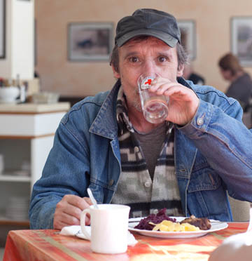 Foto: Ein Mann trink aus einem DRK-Glas am Tisch mit einem Teller Essen.